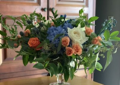 orange, white and blue flowers with greenery in pedestal container