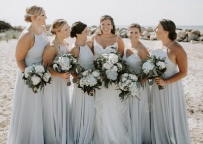 bride and bridesmaids on beach laughing with bouquets