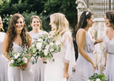 bride laughing with bridesmaids holding white greenery bouquets