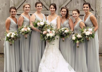 bride and bridesmaids posing with bouquets in front of barn
